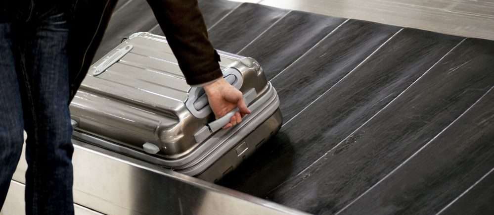 uomo mentre riprende il suo trolley dal nastro bagagli dell'aeroporto